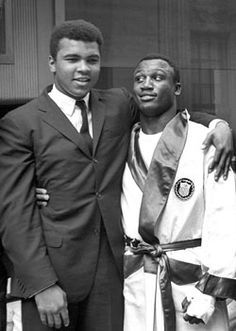 two men standing next to each other in front of a building wearing suits and ties