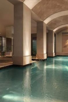 an indoor swimming pool in a large room with columns on either side and lights hanging from the ceiling