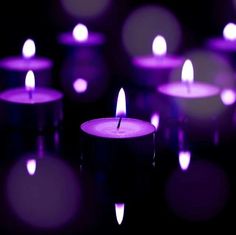 many lit candles are in the dark with purple lights around them and one candle is glowing