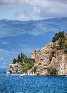 an island in the middle of water with trees on it and mountains in the background