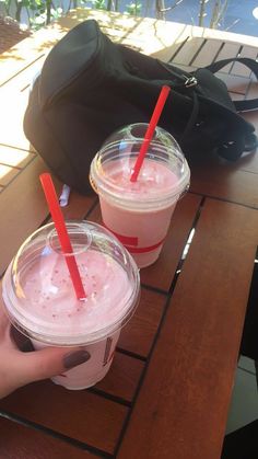 two plastic cups filled with pink liquid on top of a wooden table