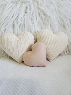 two heart shaped pillows sitting on top of a bed next to a fluffy white pillow