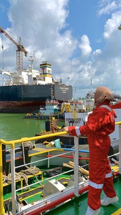 a person in a red suit standing on a boat looking at a large cargo ship