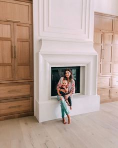 a woman holding a child in front of a fireplace