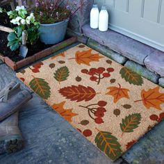 a door mat with fall leaves on it next to a planter and potted plants