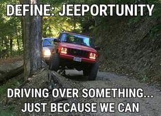 a red jeep driving down a dirt road next to a wooded area with trees on both sides