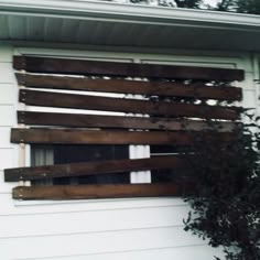 a window with wooden slats on the side of a white house next to a tree