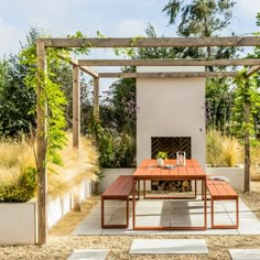 a wooden table sitting under a pergolated area with plants and trees in the background