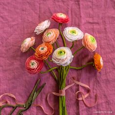 a bunch of flowers sitting on top of a pink table cloth next to scissors and ribbon