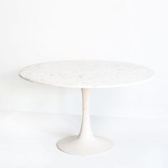 an oval marble table with white pedestals on the top and bottom, against a plain white wall