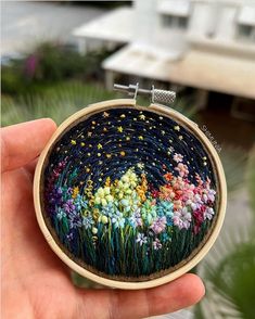 a hand holding up a small embroidery hoop with colorful flowers on the inside and outside