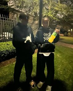 two men standing next to each other on top of a lush green field at night