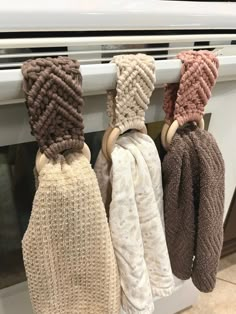 three knitted mittens hanging from the side of an oven