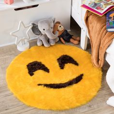 a yellow smiley face rug sitting on top of a wooden floor next to stuffed animals