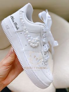 a hand holding up a white nike air force shoe with pearls on the laces