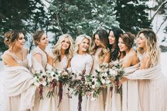 a group of women standing next to each other in front of snow covered trees and holding bouquets