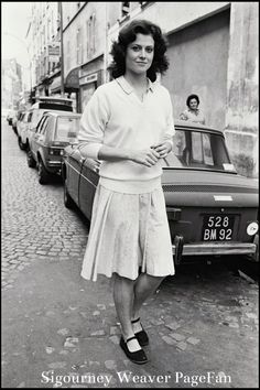 a woman standing on the street in front of parked cars, with her arms crossed