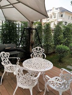 an outdoor table and chairs on a wooden deck next to a bbq with grill in the background