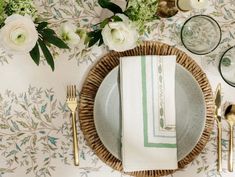 a place setting with napkins, silverware and white flowers on the wallpaper