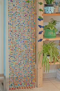 a wooden shelf filled with lots of plants next to a wall covered in colorful beads