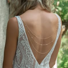 the back of a woman's wedding dress with gold chain necklaces on her neck