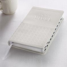 a white book sitting on top of a table next to a cup