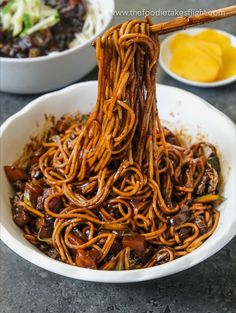 a bowl filled with noodles and meat on top of a table next to other bowls