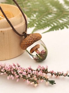 a necklace with a small mushroom inside of it on a wooden box next to flowers