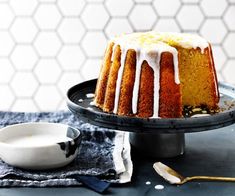 a bundt cake with icing on a black plate next to a white bowl and spoon