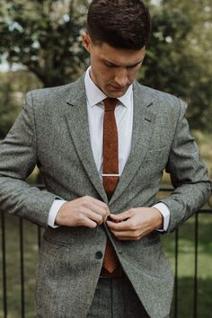 a man wearing a suit and tie standing in front of a fence with his hands on his chest