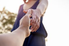 two people holding hands with one person reaching out for the other's hand in front of trees