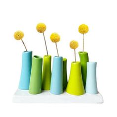 four vases with yellow flowers in them on a white surface, one is green and the other is blue