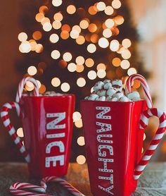 two red mugs filled with candy canes sitting on top of a table next to a christmas tree