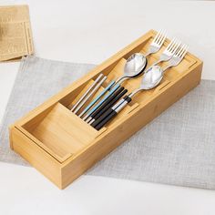 spoons, forks and knives are in a bamboo box on a tablecloth with a napkin