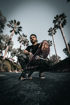 a man sitting on the ground with his skateboard in front of some palm trees