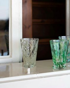 three glass cups sitting on top of a white counter next to a window sill