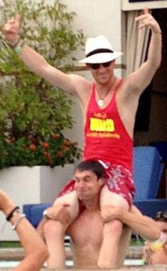 a man in a red shirt and white hat standing on the back of a swimming pool