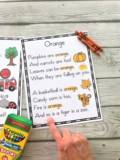 a hand pointing at an orange poem on a table with crayons and pencils