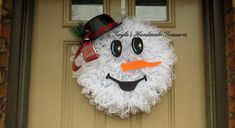 a wreath made to look like a snowman is hanging on the front door with an orange nose