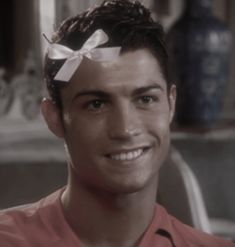 a young man with a bow in his hair smiles at the camera while wearing an orange shirt