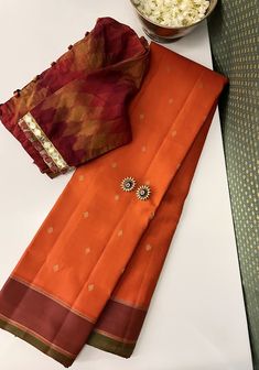 Oranges in kanchipuram silk are effortlessly sacrosanct. This pure handwoven kanchipuram silk has varying shades of oranges throughout. The body is a bright orange with simple zari woven buttis, while the pallu and border are a deeper burnt orange. The border has a green selvedge that adequately highlights the oranges and the pallu has pure zari woven stripes through it all. With numerous styling options, this saree effortlessly transitions from intimate family gatherings to grand weddings. Burnt Orange Saree, Orange Saree Contrast Blouse, Orange Kanchipuram Saree, Pearl Blouse, Kanchi Sarees, Bridal Lehenga Designs, Orange Saree