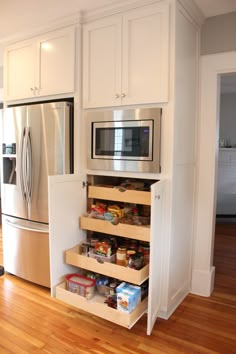 a kitchen with white cabinets and wooden flooring has an open pantry in the middle