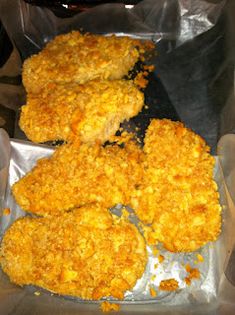 four pieces of fried chicken sitting on top of tin foil in a pan with other food items