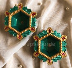 two green and gold brooches sitting on top of a white cloth