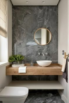 a white toilet sitting next to a wooden counter top under a round mirror in a bathroom