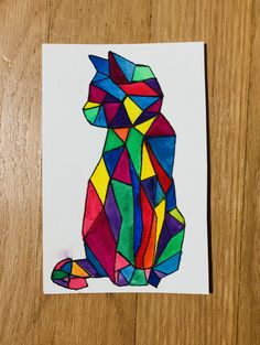 a cat made out of stained glass sitting on top of a wooden table next to a piece of paper