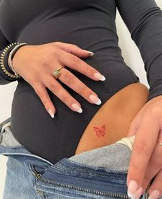 a pregnant woman's belly with a butterfly tattoo on her left side, in jeans