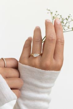 a woman's hand with a ring on her finger and flowers in the background