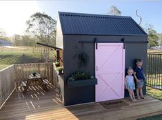 two children standing in front of a pink door on a small shed with a black roof