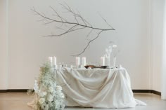 a table with candles and flowers on it in front of a tree branch that is hanging from the ceiling